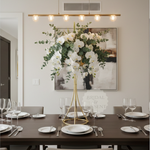 Load image into Gallery viewer, Dining room table set with plates, glasses, and a floral centerpiece on a wall with a painting.
