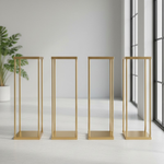 Load image into Gallery viewer, Four gold metal display stands against a white wall with a plant in the corner.

Harlow flower stand, gold wedding centerpiece stand, geometric floral riser, metal column vase, Tall centerpiece stand, wedding table decorations, heavy duty flower stand, gold pedestal stand.
