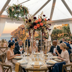 Load image into Gallery viewer, Dinner party with guests seated at a table with floral centerpieces, outdoor setting.
