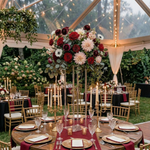 Load image into Gallery viewer, Decorative table setting with flowers and candles under a clear tent in an outdoor garden.

