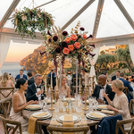 Load image into Gallery viewer, Dinner party with guests seated at a table under a clear tent, decorated with floral arrangements.

