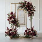 Load image into Gallery viewer, Floral arch with wedding invitation in the center against a white paneled wall.
